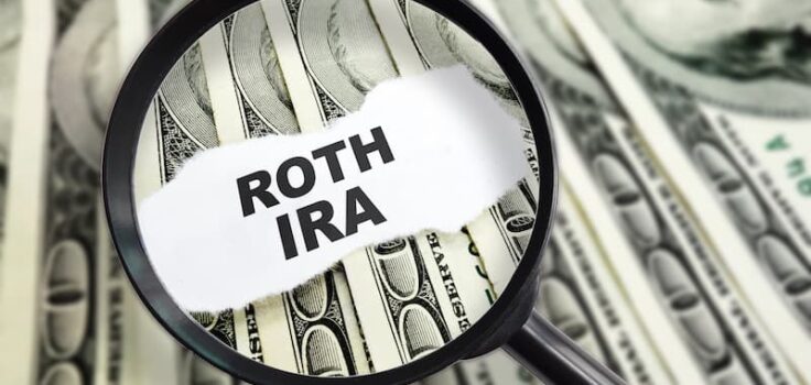 A magnifying glass over a stack of money with Roth IRA written over it. Signifying the amount of money to be saved with a Roth IRA account.