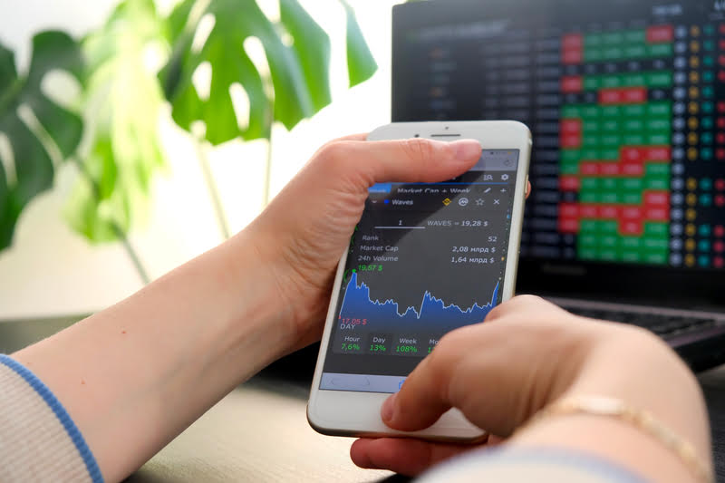 A person using a cell phone to trade cryptocurrencies on a laptop