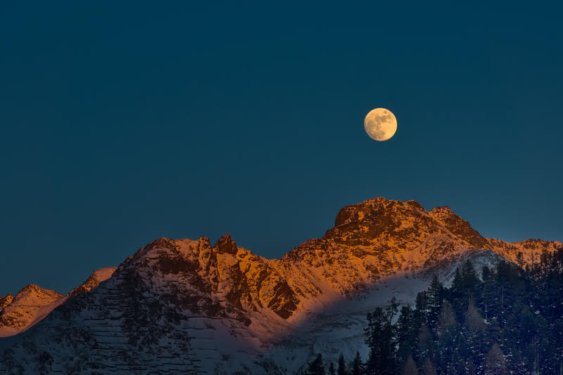 A full moon rising over a mountain range, symbolizing the rise of cryptocurrencies in the investment landscape
