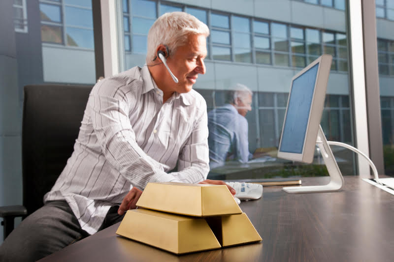 A man wearing a headset, managing precious metals investments on his computer